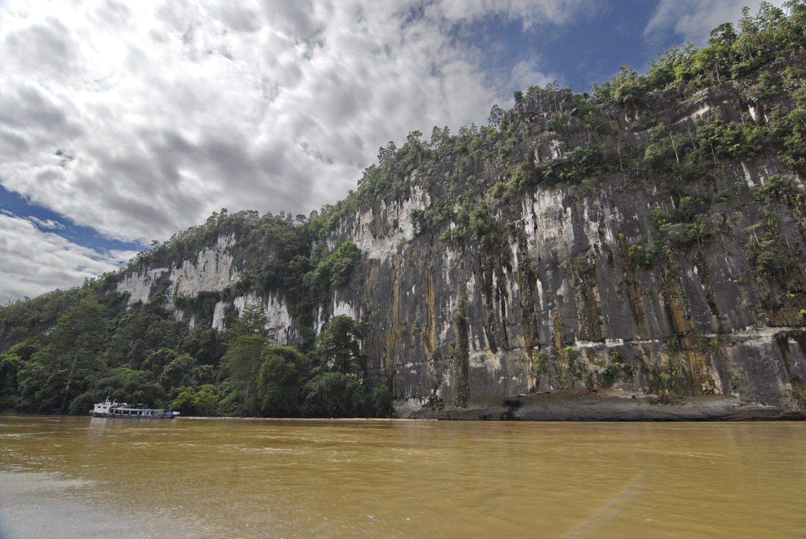 Tebing Batu Dinding di tepi Sungai Mahakam dengan sebuah kapal melintas di dekatnya